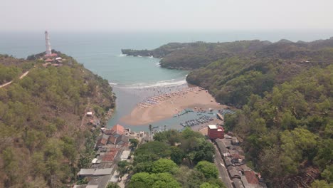 revela una toma de avión no tripulado de la bahía de baron con un faro en la parte superior del acantilado y barcos de pescadores atracados en el puerto - indonesia