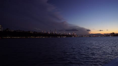 sunset skyline of new york city modern cityscape illuminated at dusk, boat approaching the city center during sunset