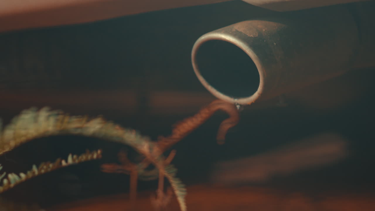 Cinematic close-up of a vehicle's exhaust pipe emitting smoke and dripping water, illustrating environmental pollution and carbon emissions