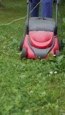 a woman is mowing grass and weeds with a lawn mower near a fence in the yard vertical video