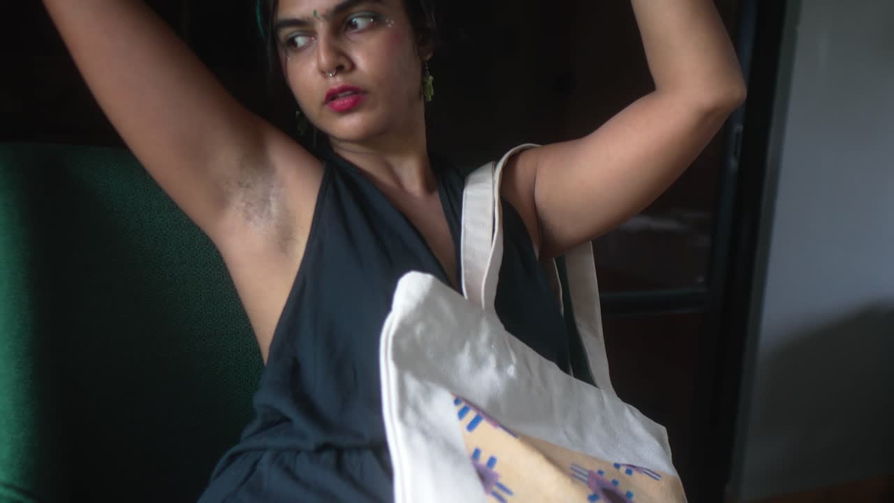 Mujer joven posando naturalmente con vello axilar visible y bolso de tela