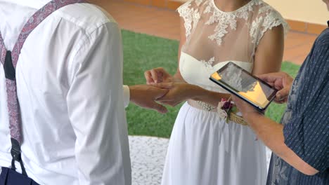 La-Novia-Intercambia-Anillos-De-Boda-En-La-Celebración-Mientras-El-Sacerdote-Lee-De-La-Tecnología-De-La-Mesa