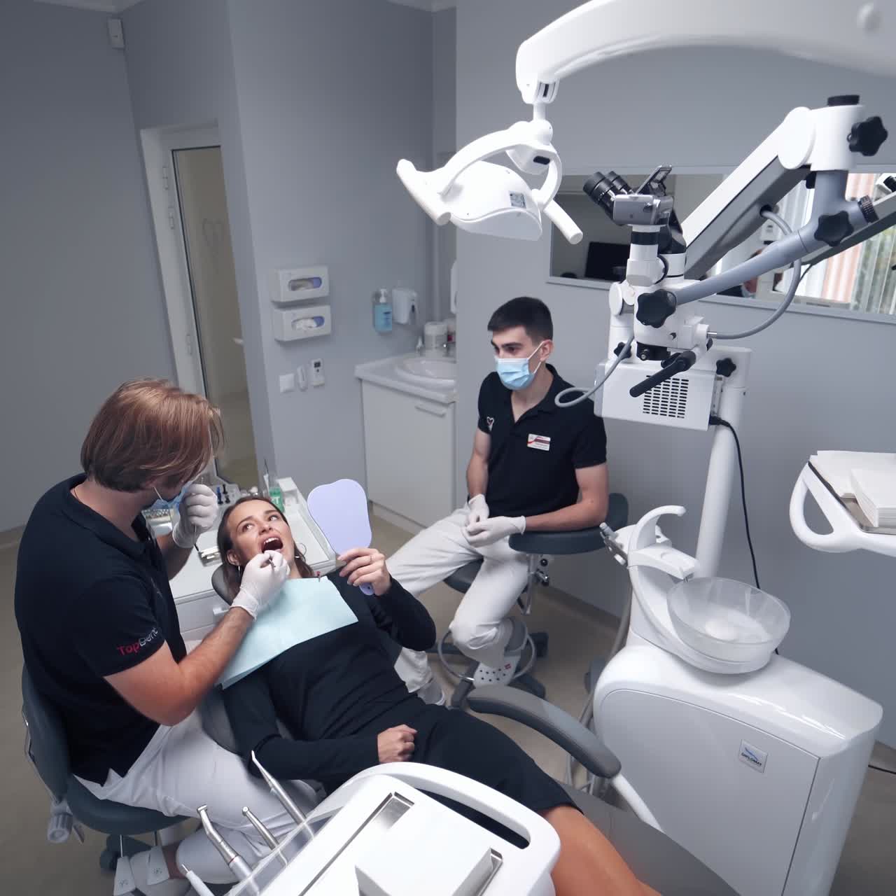 Female patient laying in dentist chair. Stomatologist and his assistant treating woman's teeth in modern clinic.