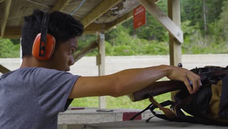 Side-Portrait-Of-An-Asian-Man-Puts-On-Protective-Ear-Muffs-And-Hold-A-Karabiner-98k-At-The-Shooting-Range