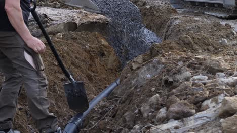 static shot of a man looking at a machine pouring gravel on a pipe, making drainage, for his future house, in ostrobothnia, finland