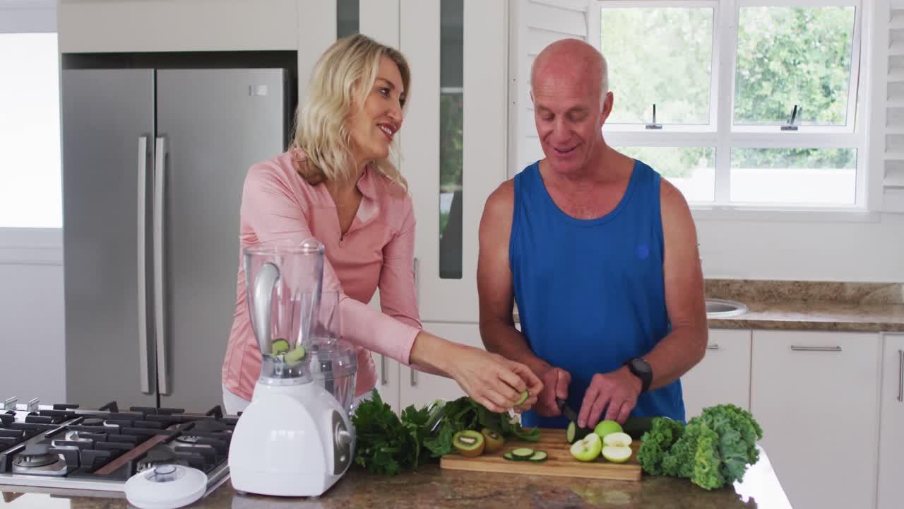 Homem e mulher caucasianos idosos preparando bebidas saudáveis de frutas e vegetais em casa.