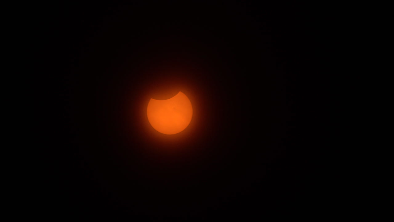 Partial phase of a solar eclipse resembling a jack-o-lantern moves across a hazy sky