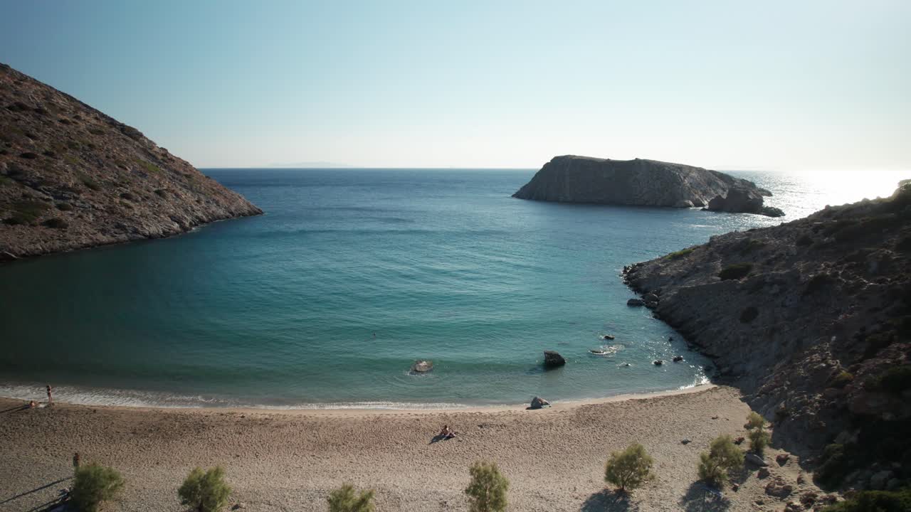 Drone ascends above calm peaceful varvarousa beach cove in syros greece, tilt down to reveal sun bathers