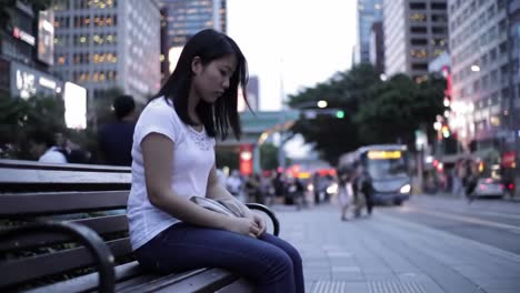 young woman sitting alone on a bench in a city at dusk