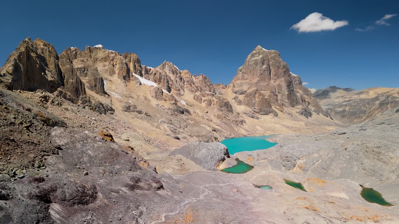 Aerial flyover captures the dramatic peaks, arid ridges, and turquoise glacial lakes of the spectacular Cordillera Huayhuash trek with winding path in the Peruvian Andes