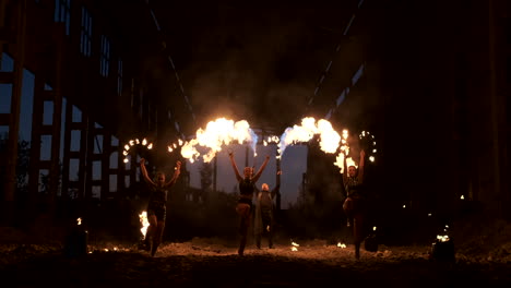 four women in leather clothes with fire dance and show fire show a man with a flamethrower in the back plays with the flame in slow motion