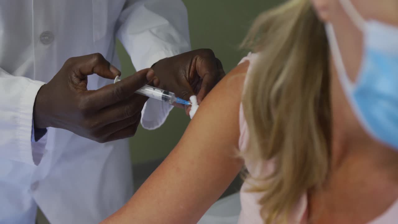 paciente caucásica con máscara facial sentada en una cama de hospital recibiendo una inyección