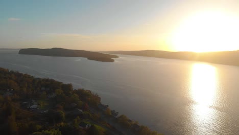 Drohnenaufnahme-Eines-Atemberaubenden-Sonnenuntergangs-über-Dem-Wasser,-Der-Einige-Grundstücke-Am-Seeufer-Enthüllt,-Als-Die-Drohne-Zurückfährt