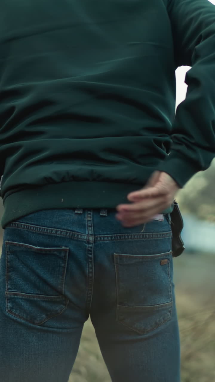 초록색 재과 청바지를 입은 남자의 근접한 모습, 그는 야외 환경을 통해 조심스럽게 움직이는 것처럼 뒤에서 볼 수 있습니다.