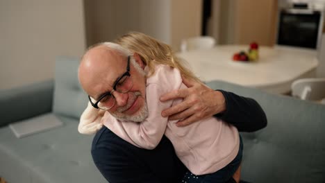 Little-granddaughter-hug-old-elder-grandfather-at-home