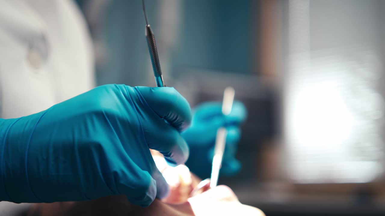 un dentista con guantes de goma sostiene las herramientas de limpieza de dientes y examina los dientes de un paciente