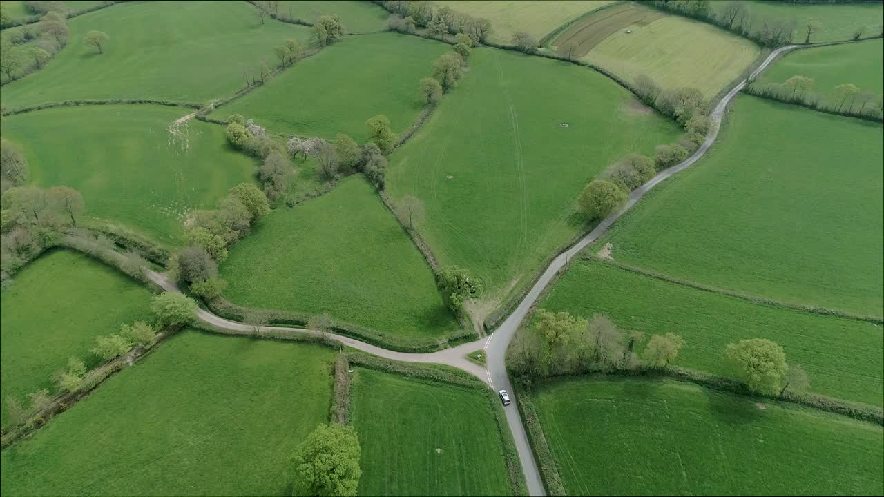 la antena de un coche plateado recorre una carretera rural inglesa y pasa por un cruce triangular