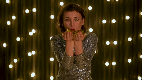 young beautiful woman blowing gold glitter confetti and looking at camera