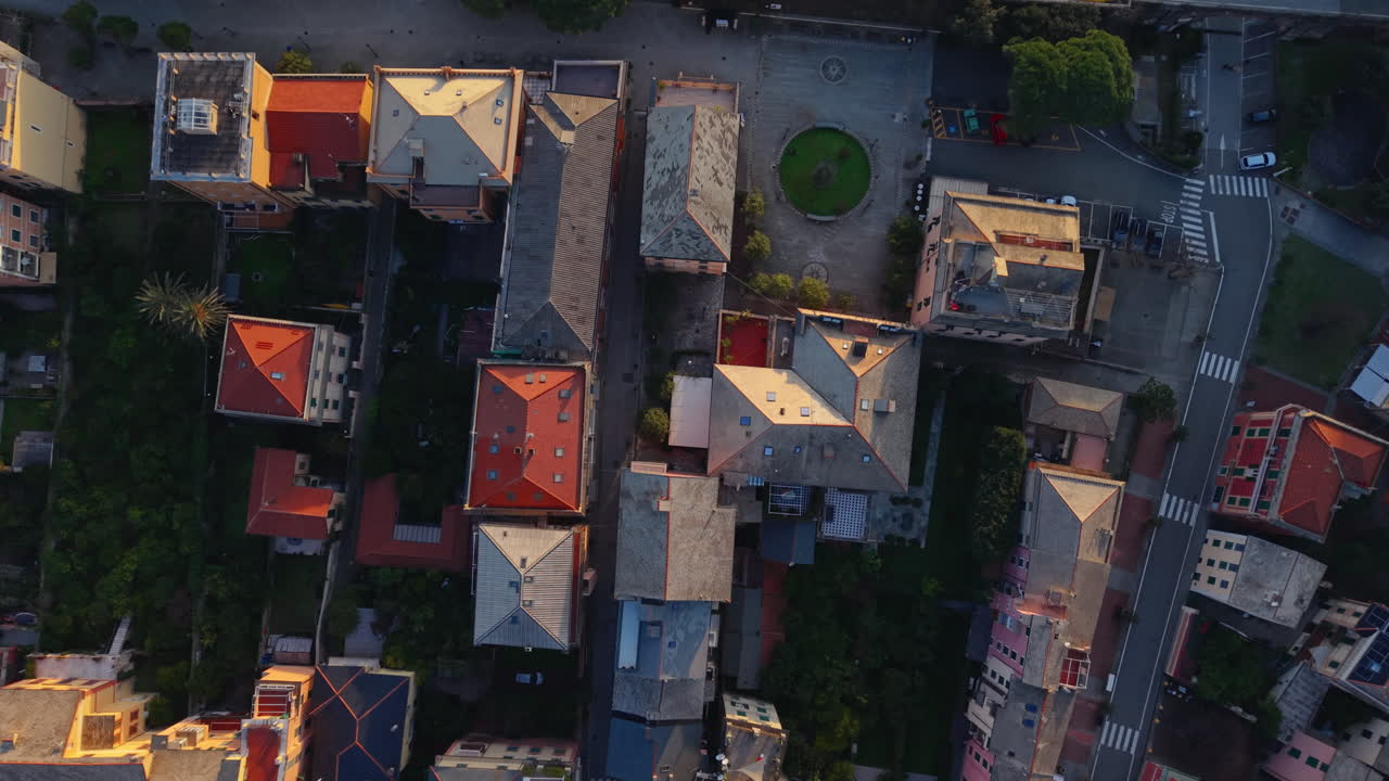 Drone rises above Bonassola rooftops, revealing beach, waves and sea at sunset