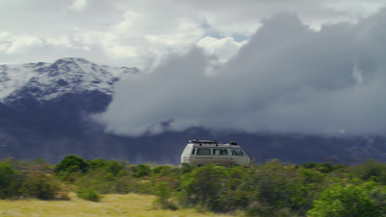A van drives down a road that runs by a mountain