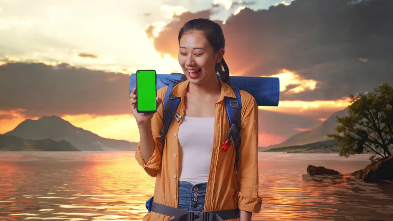 turista sonriente con mochila y teléfono de pantalla verde en el lago sunset