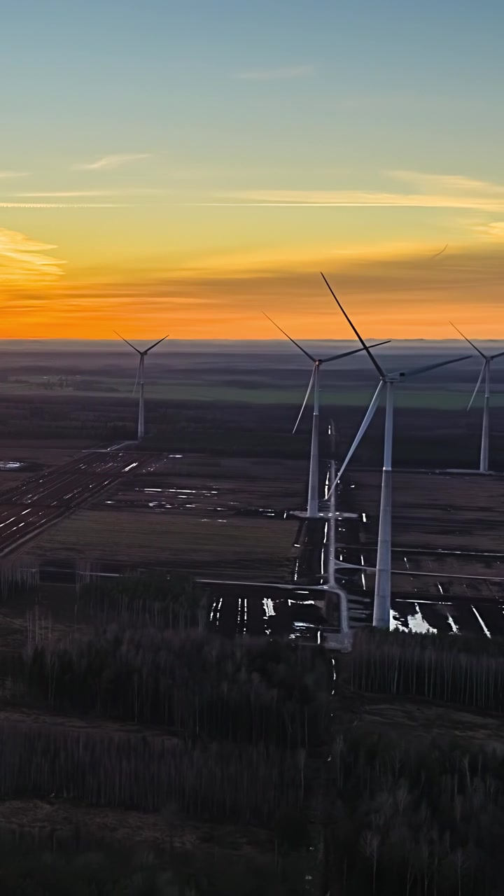 Vindmøller snurrer over åbne marker ved solnedgang og genererer vedvarende energi i et landligt landskab.