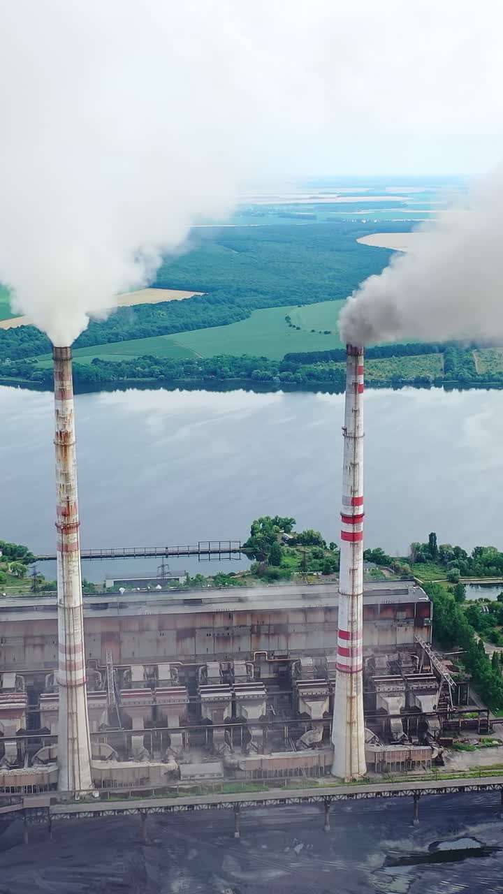Harmful industry on river background. Factory pipes with smoke pouring into the atmosphere. Air pollution among beautiful nature. Vertical video