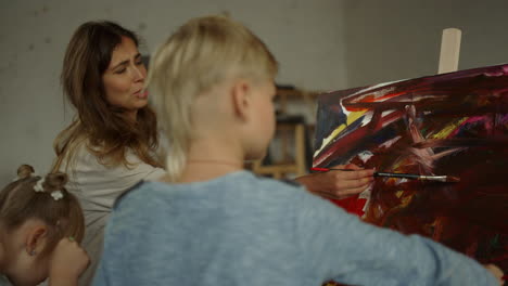 familia inspirada creando obras de arte en el interior. joven pintora enseñando a los niños.