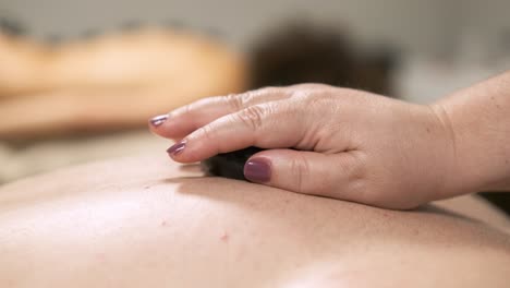 masseuse gently placing a warm stone on a client's back during a relaxing massage session