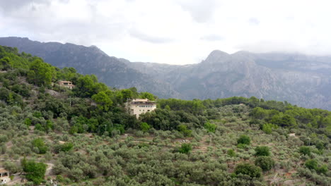 AERIAL:-Towards-House-in-Jungle-Mountains-on-Tropical-Island-Mallorca,-Spain-on-Sunny-Day-Vacation,-Travel,-Sunny,-Waves