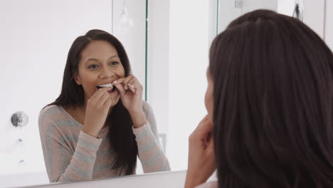 reflection of woman using dental floss in bathroom mirror