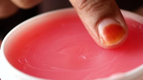 close-up of a pink lip balm being applied with a finger