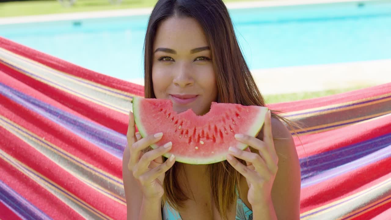 비키니 를 입은 기쁜 여자 가 수박 조각 을 먹고 있다