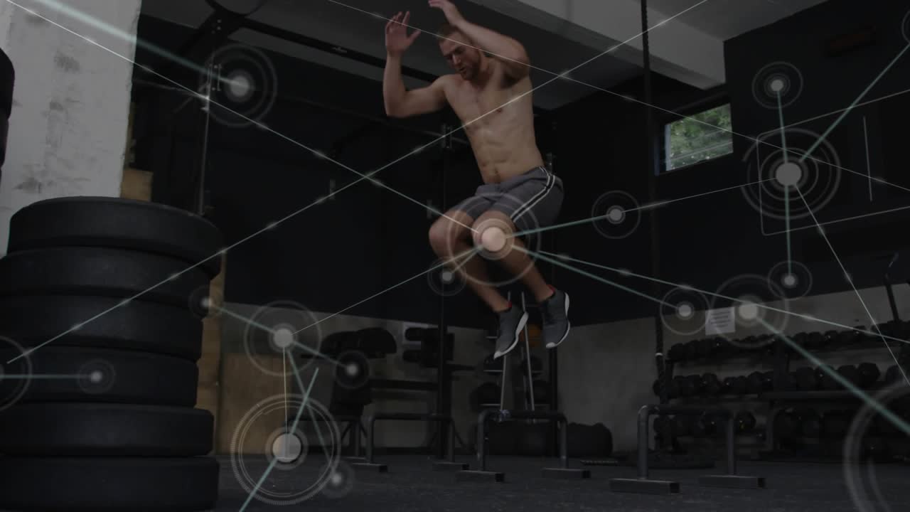 Vertical video: Starting shirtless man doing plyometric jumps in gym near plates, overlay training