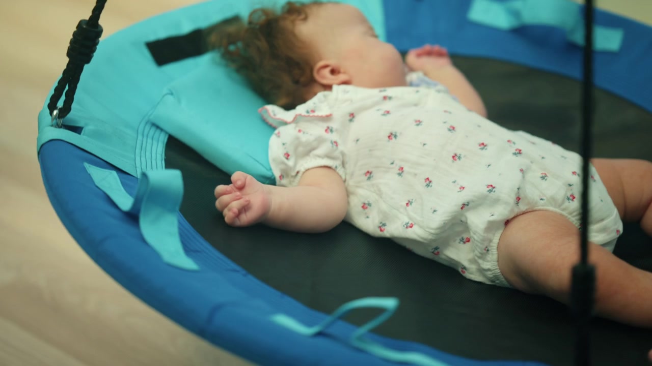 Infant child resting calmly indoors, enjoying a quiet nap in a comfortable blue and black hanging swing