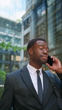 vertical video shot of serious young businessman wearing suit talking on mobile phone standing outside offices in the financial district of the city of london uk shot in real time 1
