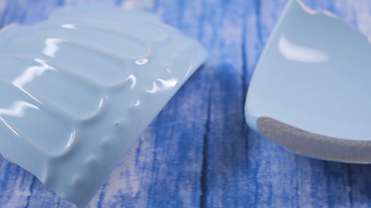 Broken Light Blue Ceramic Plate Pieces on Blue Wooden Surface