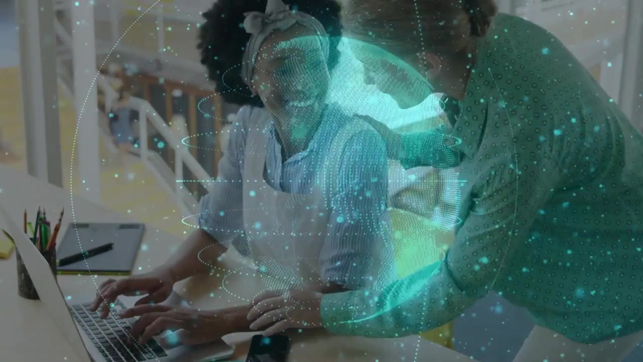 Seated worker typing on laptop activating globe overlay while peer leaning over guiding tech review