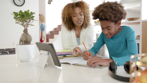 african american mother helping her son with homework using tablet in kitchen, slow motion
