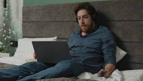 boy is watching videos on laptop while eating popcorns on the bed in bedroom