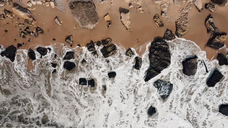 top view of rocky beach with crashing waves in nazare, portugal