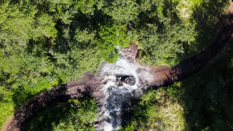 Adventure-quadbike-rider-splashing-through-creek-during-trail-drive,-top-down