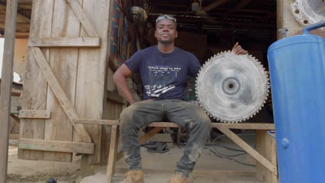 african saw repairman poses at closeup camera at traditional metal working place