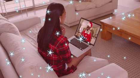 animación de nieve cayendo sobre una mujer biracial en una llamada de video portátil con papá noel en navidad