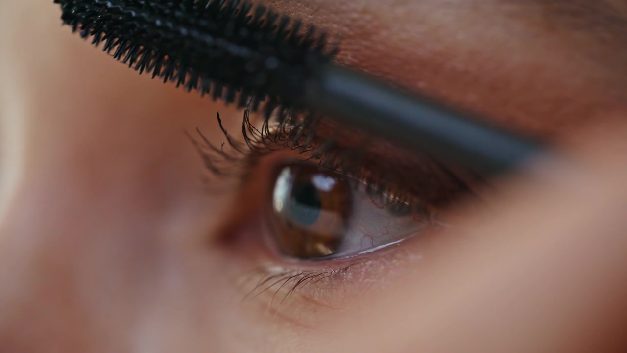 Primo piano di una donna che si trucca gli occhi con lo scovolino del mascara. Donna che applica cosmetici.