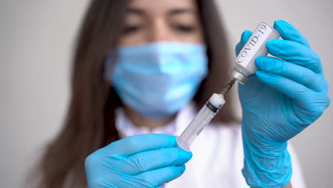 female doctor wearing medical gloves filling a syringe with a vaccine for covid 19