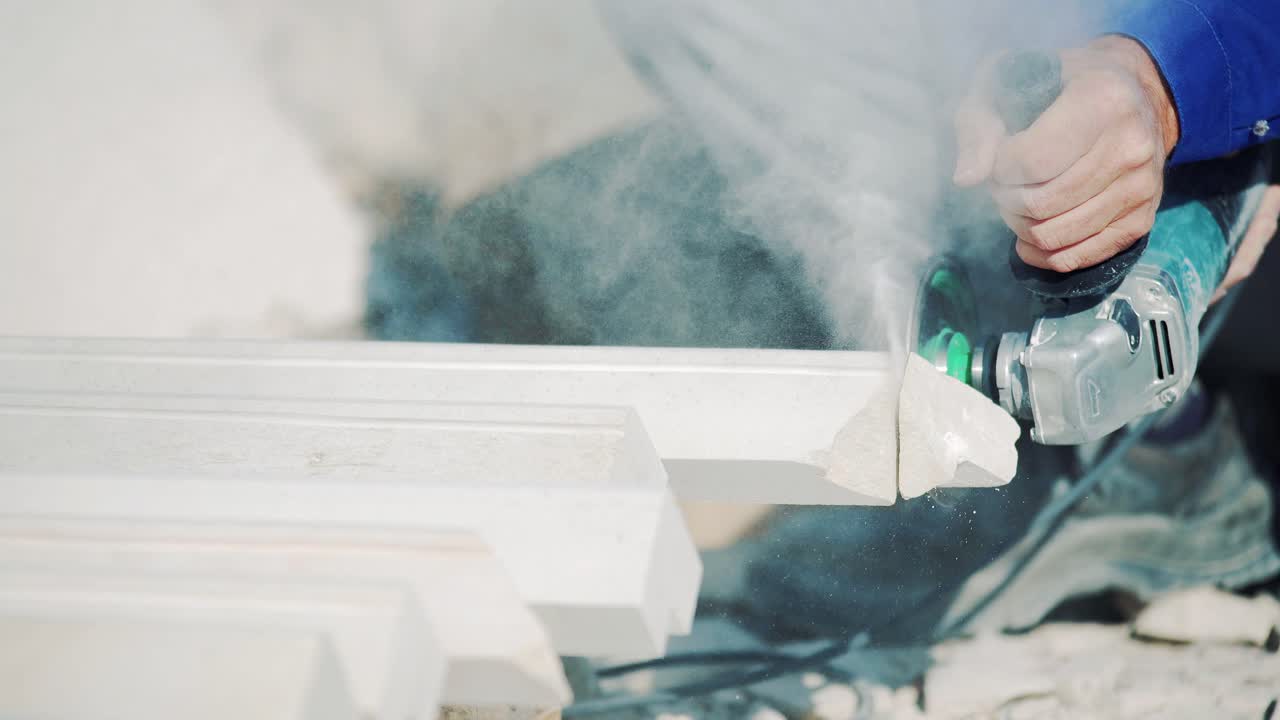 Worker cuts stone with an angle grinder. Stone dust from the work of the saw. Factory of decorative processing of sandstone