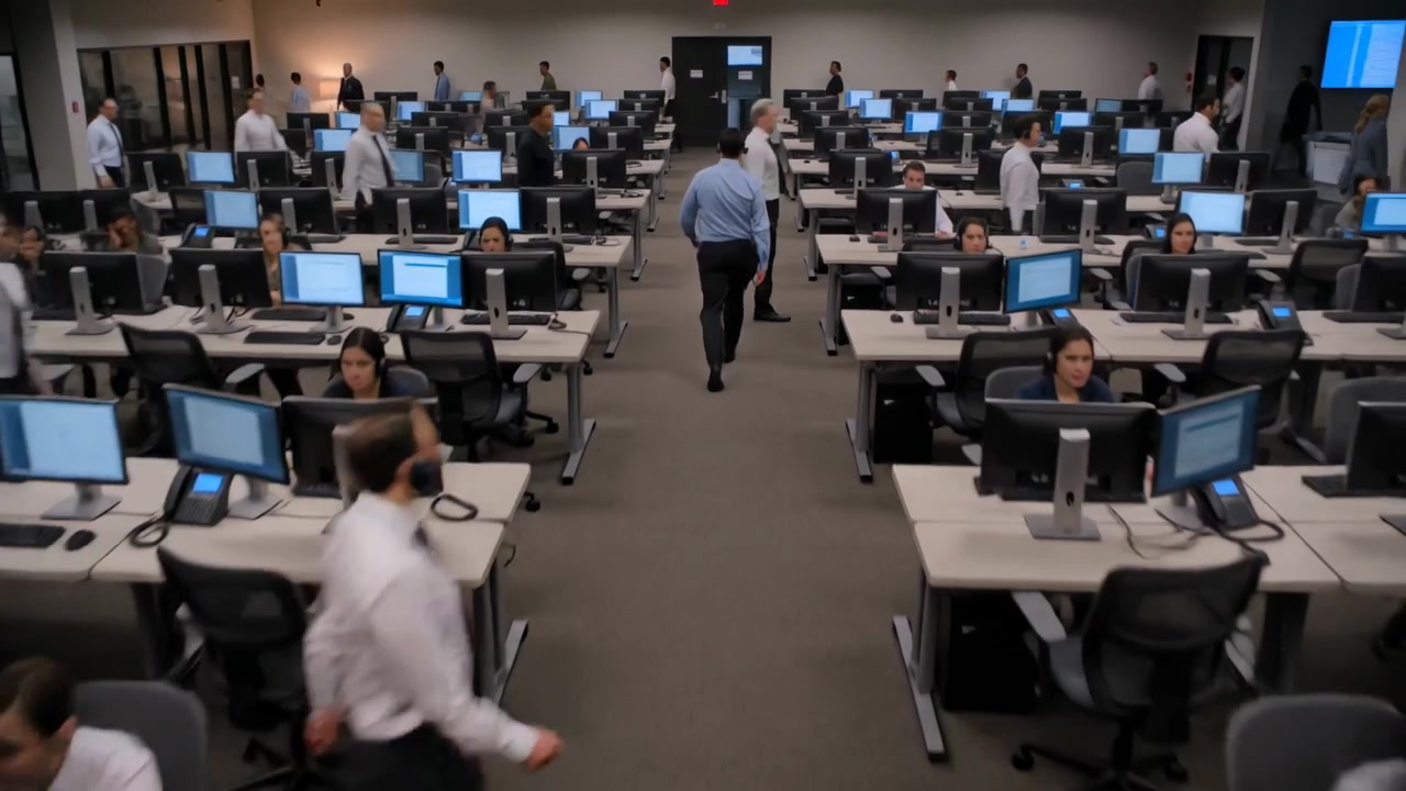Entering from far doorway, walking employee in blue shirt moving down aisle at office with monitors