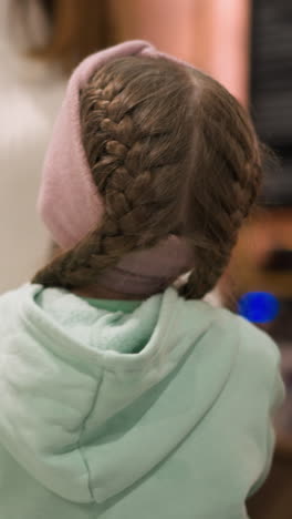 vista de cerca de una niña en una chaqueta verde menta y gorra rosa, extendiéndose para abrazar a un adulto en el borde de la pista de hielo
