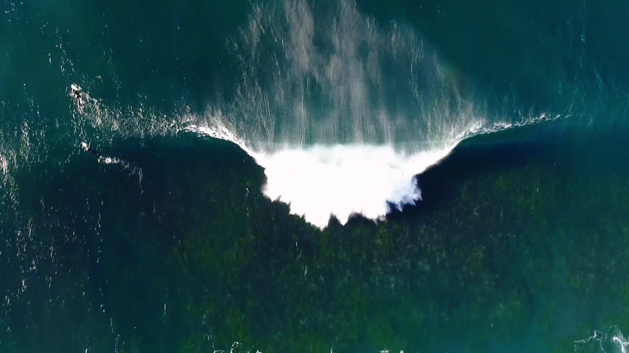 Drone shot of surfers waiting in vibrant blue lineup as wave rolls toward shallow reef break zone